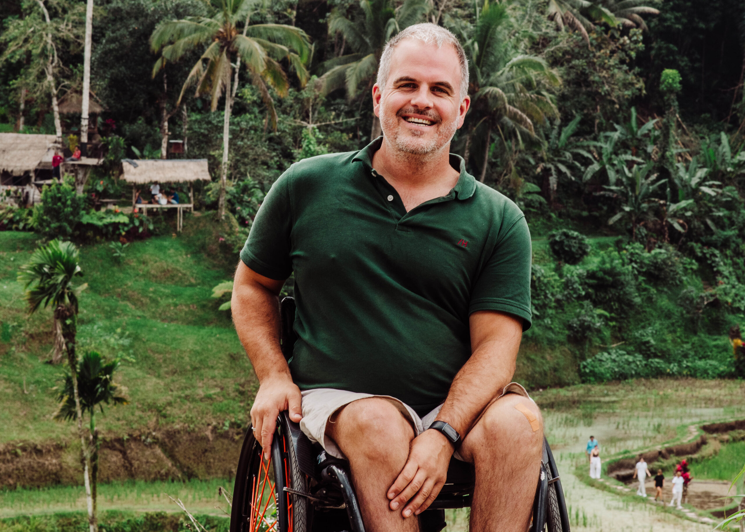 Lachende man in groen shirt in rolstoel voor Indonesisch landschap. Dwarslaesie. Chronische pijn.