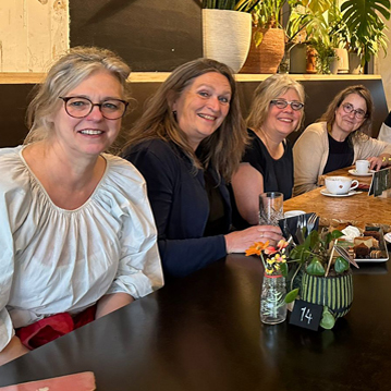 Vier lachende vrouwen aan een cafétafel kijken in de camera